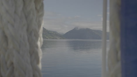 calm panning video filmed on board of a car ferry in norway going in between the fjords filming the mountains and sea or lake on a sunny cloudy day with part of the ship and rope in the foreground log