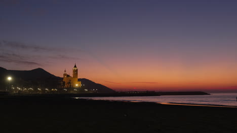 Red-sunset-twilight-coast-with-a-church-silhouette-of-hills-and-birds-flying,-man-walking-his-dog