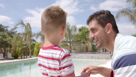 Happy-caucasian-father-and-son-talking-at-swimming-pool-at-beach-house
