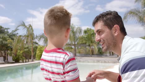 padre y hijo caucásicos felices hablando en la piscina de la casa de la playa