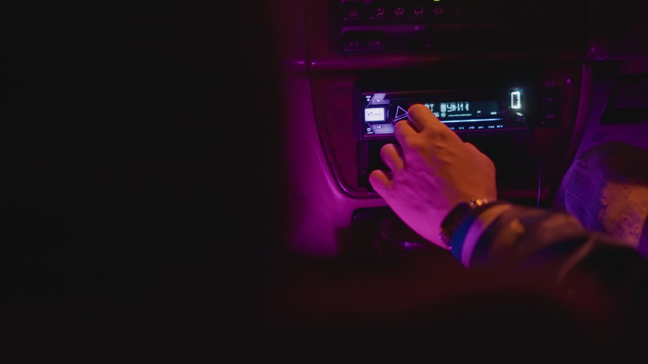 늦은 밤 라디오 방송국에서 수동으로 채널을 맞추고, 마젠타 색상의 내부 조명이 빛나며, 손가락으로 다이얼을 돌리고, 빈티지 튜너 디스플레이가 보이고, 손목 팔찌가 보이고, 여행 동반자가 노래를 찾고, 야간 근무자가 주파수를 변경해요.