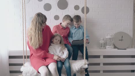 mom-and-daughter-ride-on-swing-near-sons-playing-on-tablet