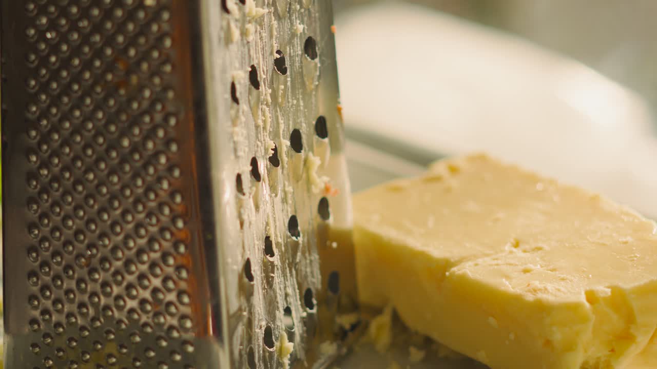 Slow Pan Across and Up Freshly Grated British Mature Cheddar Cheese Resting on Side Next to Grater in Soft Evening Light. Rustic Classic Food Setting with Cooking Ingredients