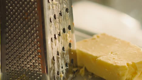 slow pan across and up freshly grated british mature cheddar cheese resting on side next to grater in soft evening light. rustic classic food setting with cooking ingredients