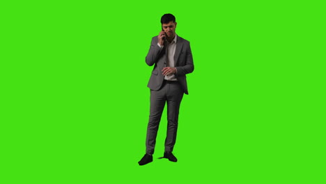 full length shot of frustrated businessman talking on mobile phone standing against green screen studio background