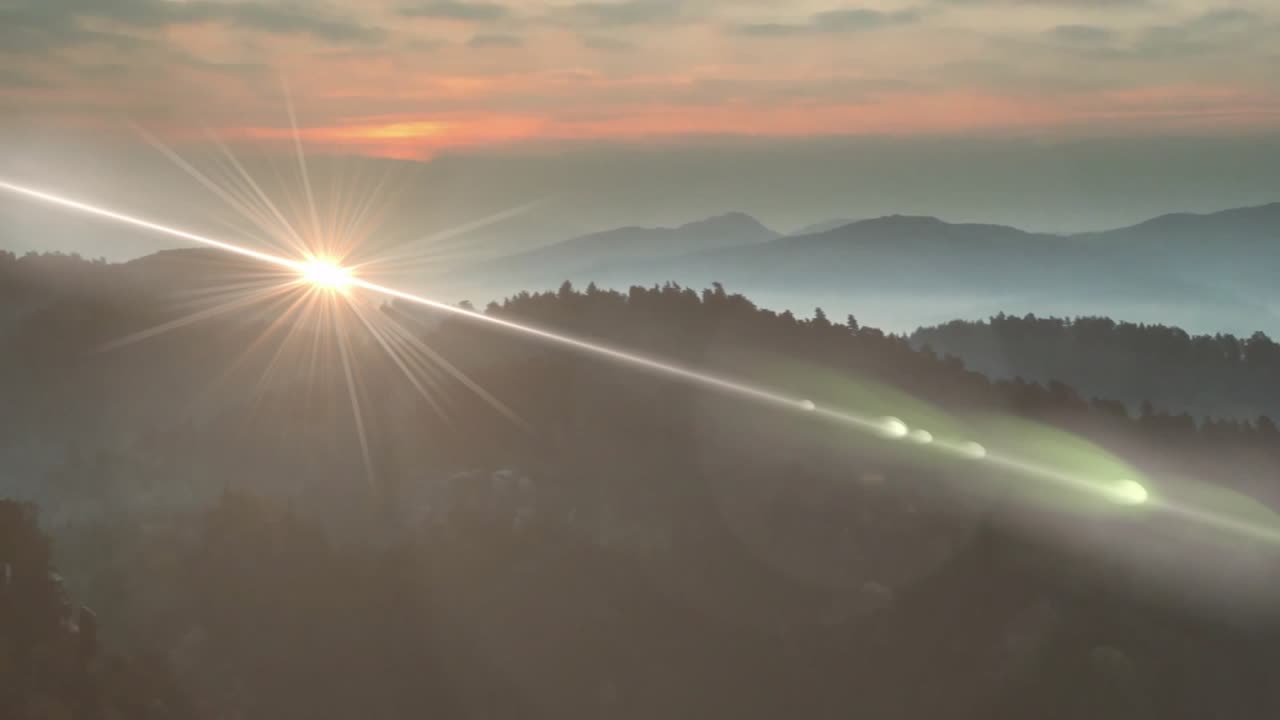 Orange glow over hills starting sun rising producing lens flare lighting misty ridge silhouettes