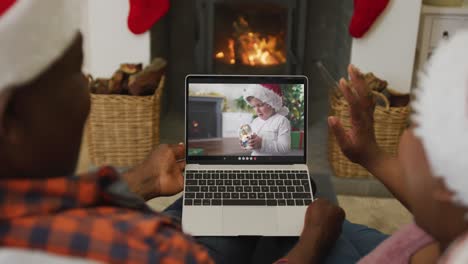 Pareja-Afroamericana-Con-Gorros-De-Papá-Noel-Usando-Una-Computadora-Portátil-Para-Una-Videollamada-Navideña-Con-Un-Niño-En-La-Pantalla