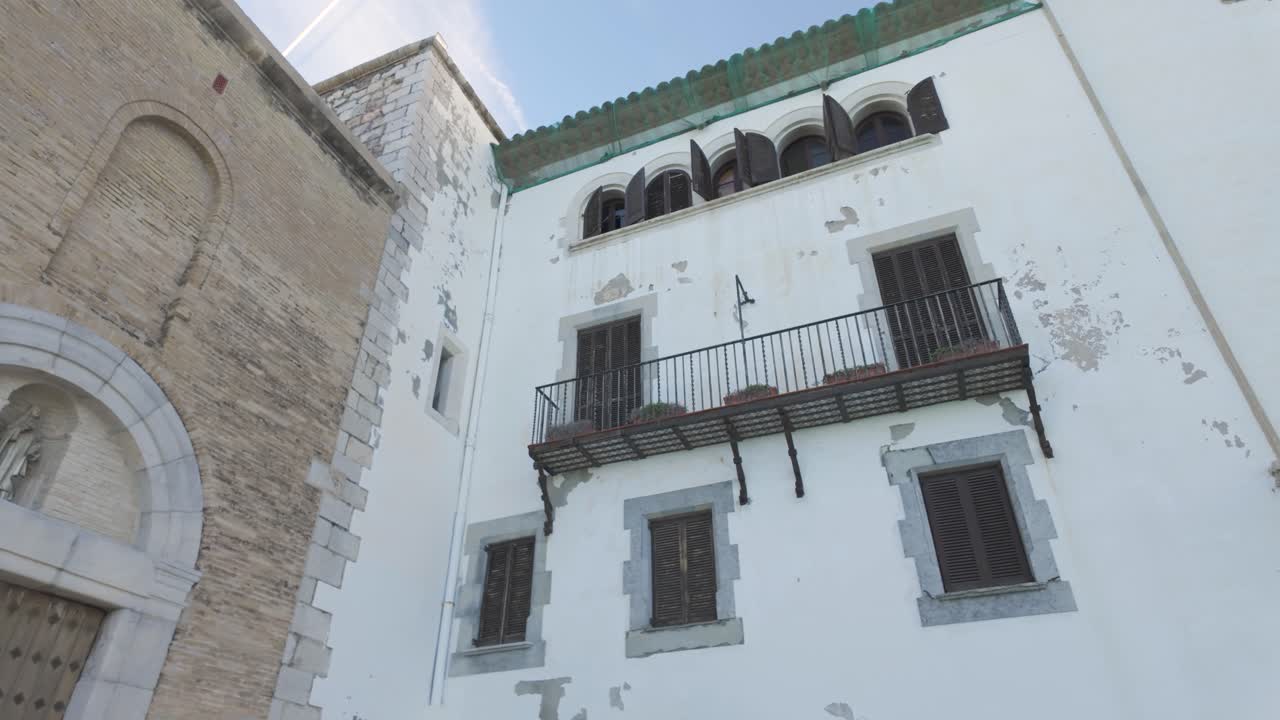 Smooth establishing right of Carrer de Fonollar in Sitges, a quaint historic street with Mediterranean charm old painted whitewash buildings