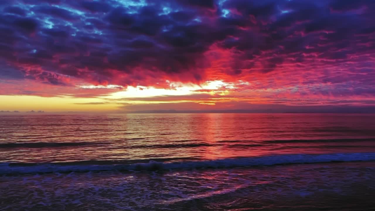 hermosa puesta de sol del océano con nubes rosadas, violetas y azules y olas suaves