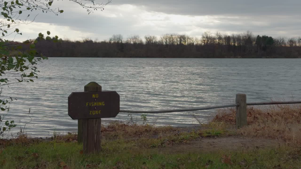 A no fishing zone sign near a lake on a cloudy day