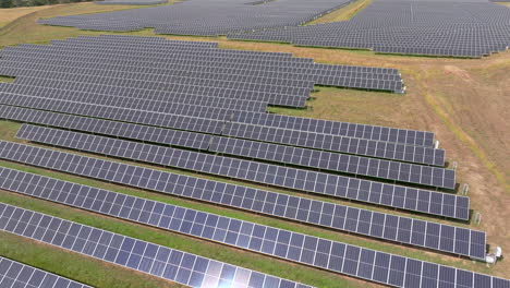 Aerial-fly-over-view-of-large-solar-farm-with-many-rows-of-solar-panels-creating-green,-renewable-energy-to-replace-fossil-fuels-and-to-power-clean-transition-to-fight-climate-change