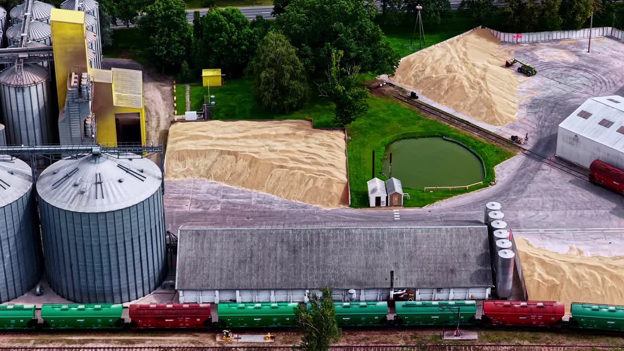 Aerial footage of trains waiting at a warehouse to transport piles of grain