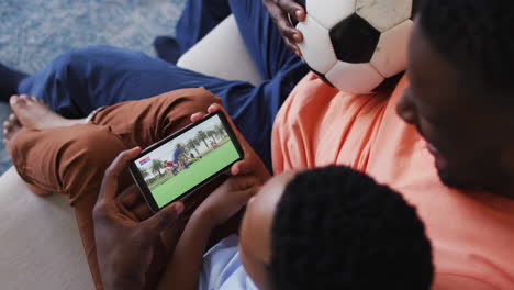 composite of father and son at home watching hockey match on smartphone