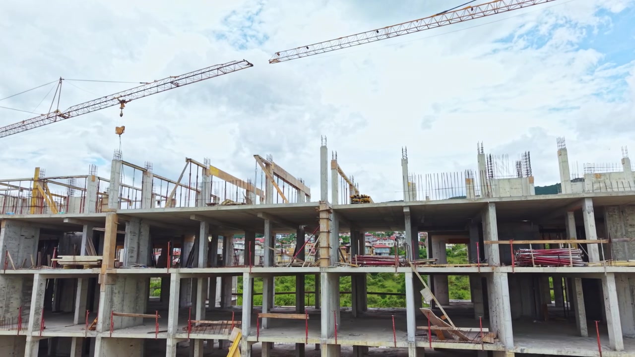 Construction progress of a building with cranes and workers at a site under cloudy skies in a town
