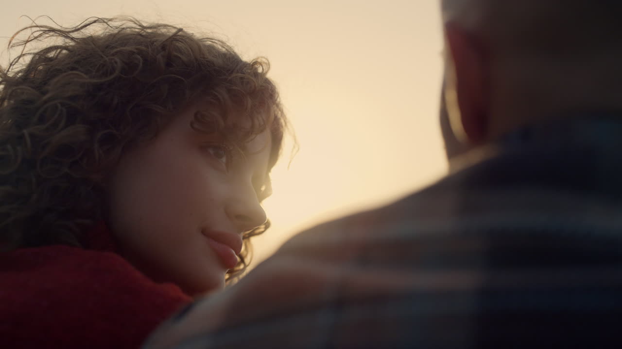 Coppia affettuosa che si frequenta in spiaggia al tramonto. Ragazza che guarda il ragazzo con amore.