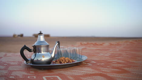 close-up-to-tea-and-empty-glass-on-red-ground-with-stunning-desert-landscape-sand-dunes-in-blurred-background