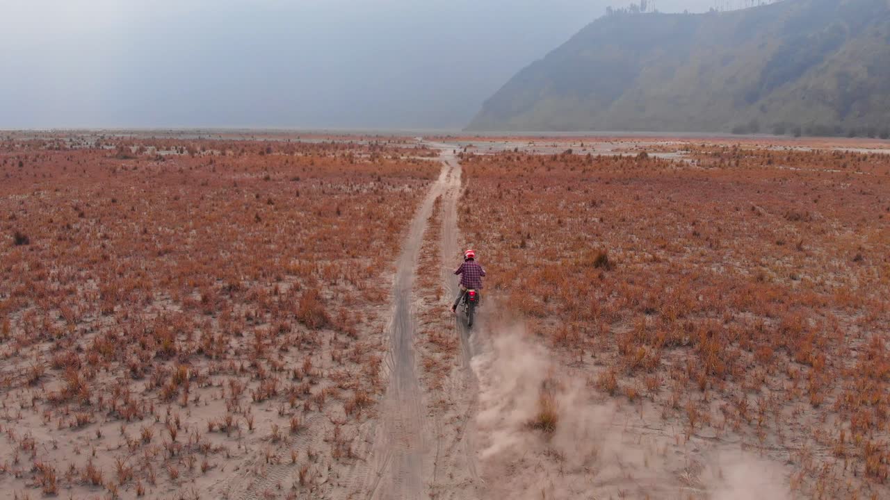 Dirt bike races through dusty volcanic sand at dawn. Indonesia, East Java