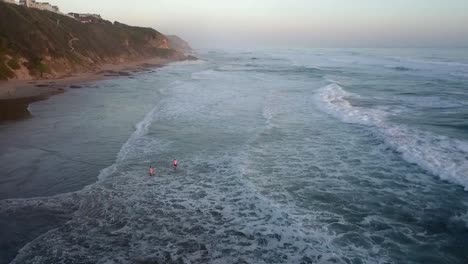 dos niños con boogie board juegan en las olas de la playa, luz aérea nocturna