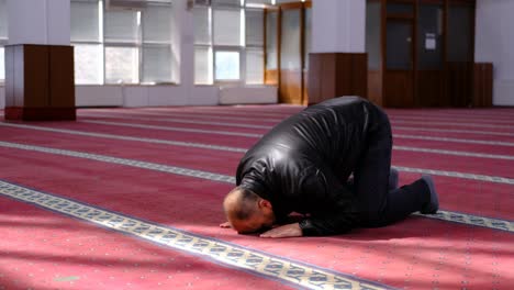 older man kneels in prayer in mosque