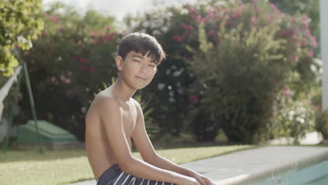 happy boy sitting on poolside, smiling and squinting from sun.