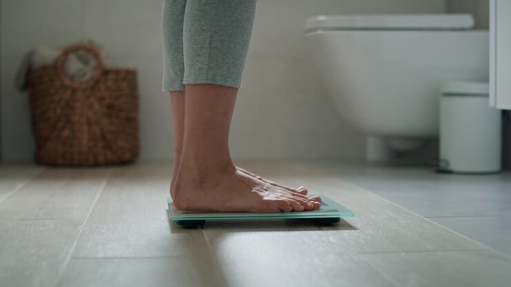 Legs of unrecognizable woman stepping on the bathroom scale.