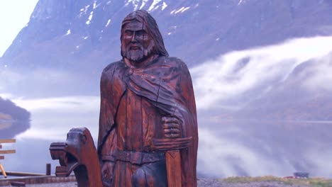 a wooden viking statue stands in front of a foggy fjord in norway