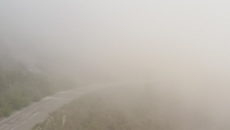 drone view of windy road on side of mountain vanishing into clouds