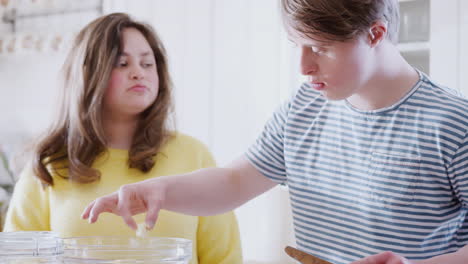 young downs syndrome couple adding butter to cake recipe they are baking in kitchen at home