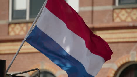 red white and blue dutch flag waving on a moored boat in heerenveen. symbol of national identity and patriotism, with classic architecture in the background