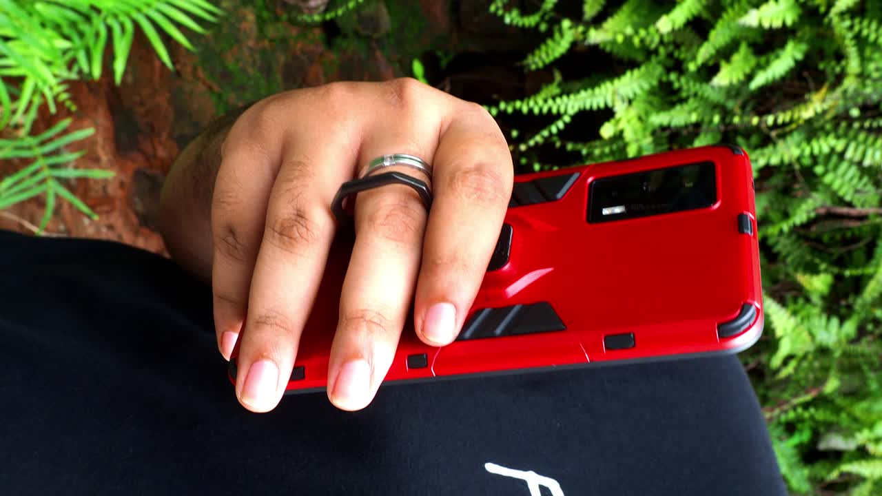 Video verticale: Primo piano estremo delle mani di un uomo irriconoscibile che digita un messaggio online usando un telefono cellulare mentre è in piedi. Vista ravvicinata della mano dell'uomo che usa il telefono e foglie verdi sullo sfondo.