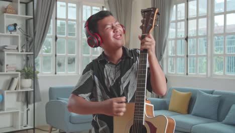 funny asian boy playing guitar, sing a song and dancing at living room