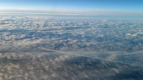 vista increíble desde la cabina de un avión que vuela alto por encima de las nubes dejando un largo rastro de aire de vapor de condensación blanco en el cielo azul
