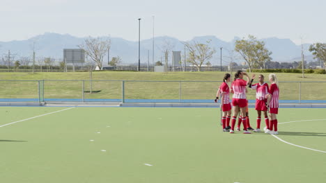 female hockey players celebrating goal on outdoor field with goalie watching