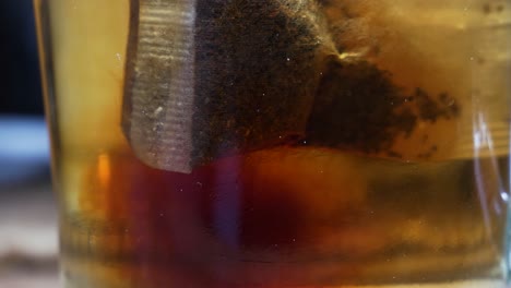 tea bag inside transparent tea cup made of glass with leafs and making water brown in close up