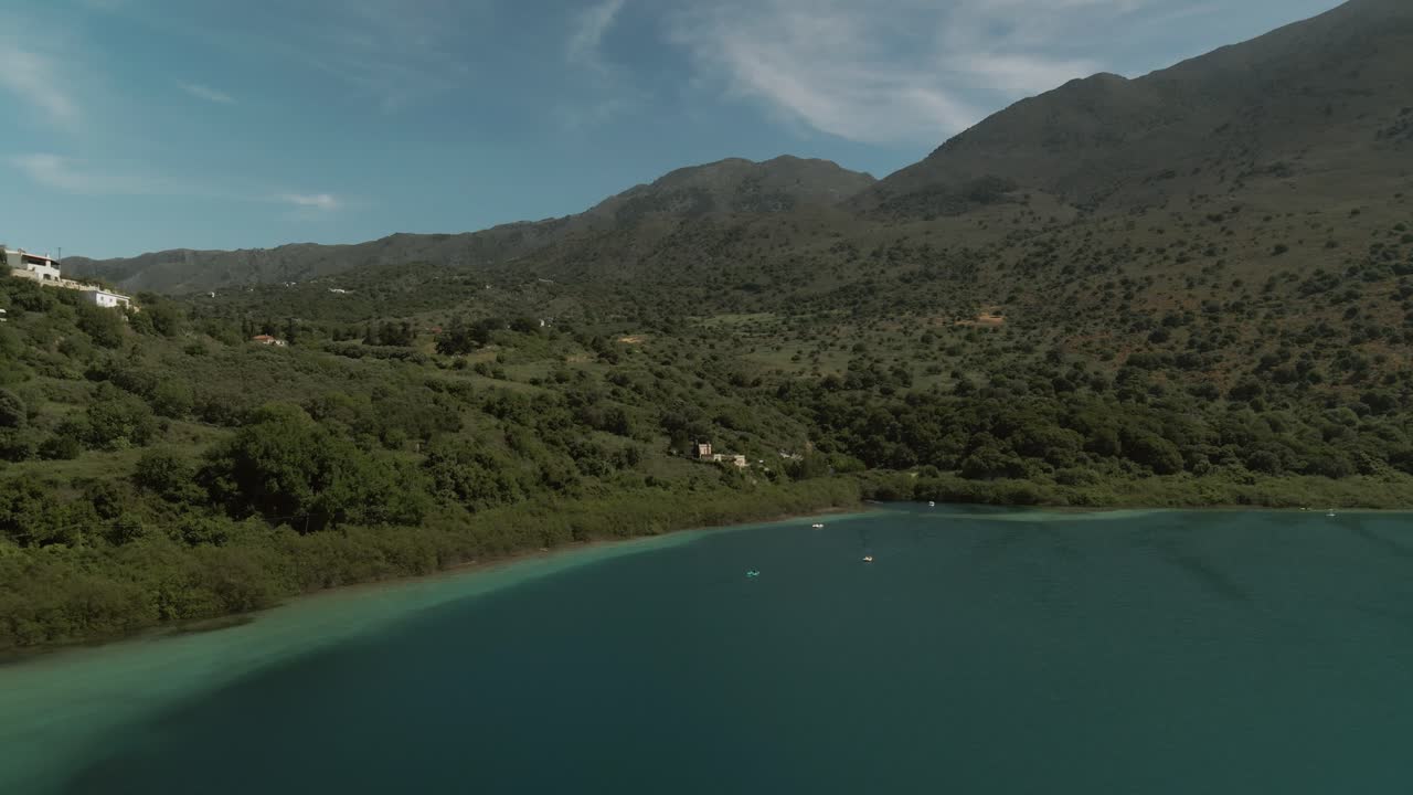 Aerial photo capturing Lake Kournas with forested hills and sparse rural buildings under soft clouds and clear skies on Crete in Greece