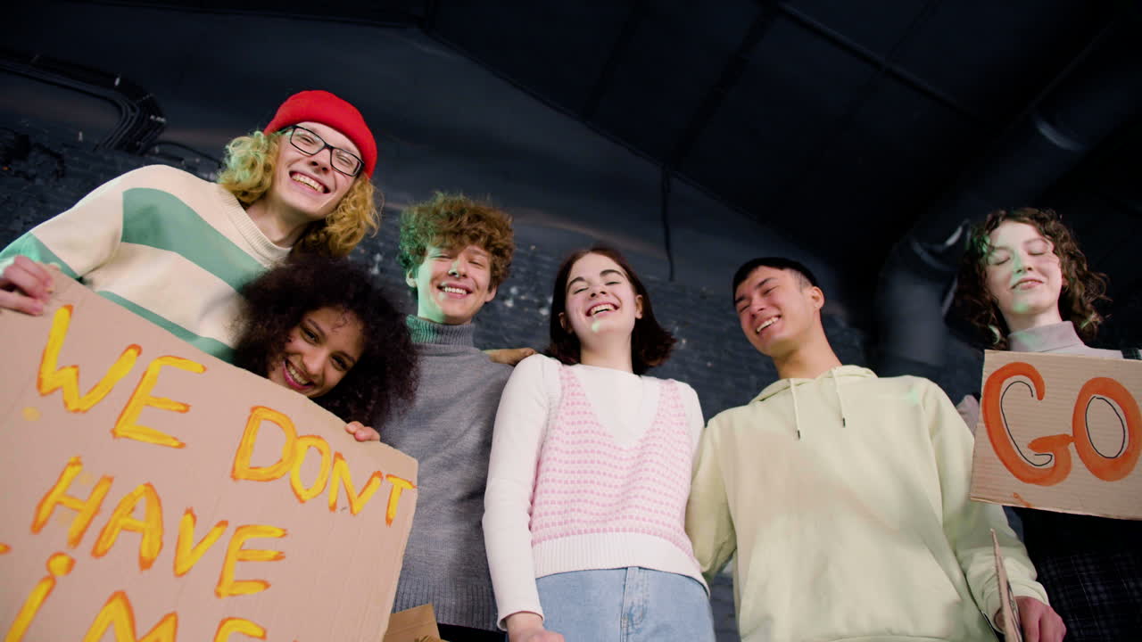 골판지 플래카드를 들고 카메라를 보며 웃는 행복한 젊은 환경 운동가들의 아래에서 보기