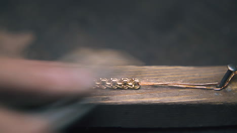 goldsmith grinds bracelet on wooden gutter at table closeup