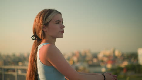 joven de pie al aire libre con las manos en la barandilla de hierro, mirando pensativo en la distancia bajo la cálida luz del sol, el paisaje urbano borroso en el fondo