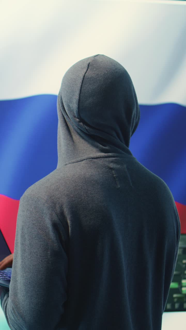 Hacker con felpa con cappuccio che digita su un portatile con sfondo con bandiera russa