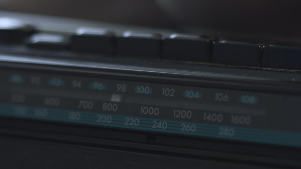 Närbild av en radiofrekvensskala med numrerade markeringar, mjukt turkost inslag, svagt ljus, precis tuner