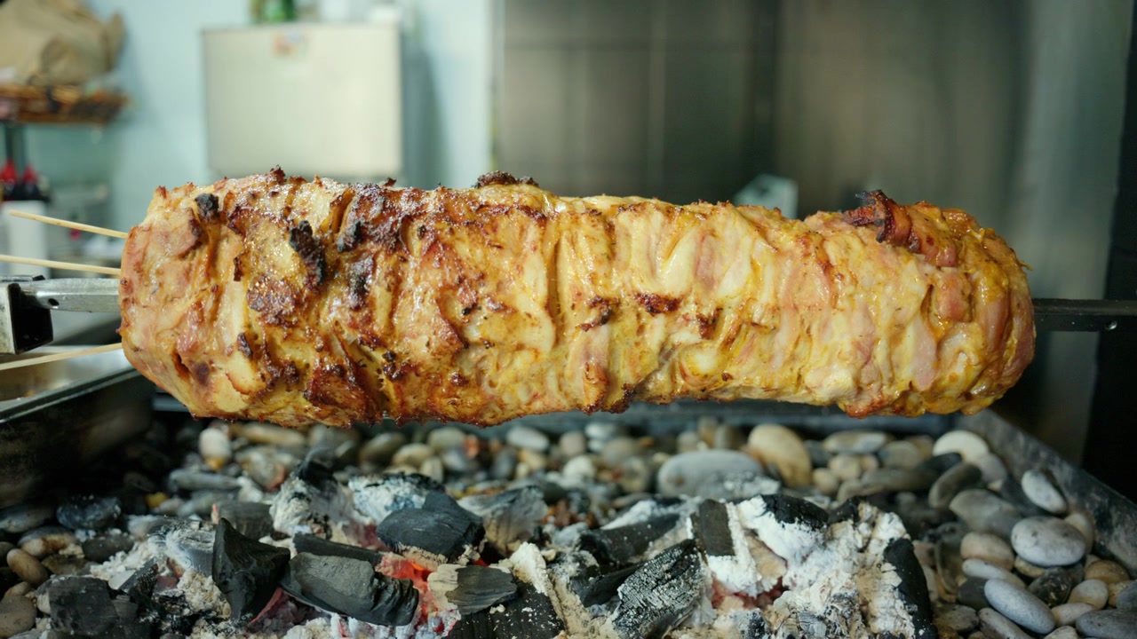 Carne per gyros che arrostisce lentamente su uno spiedo verticale su carboni ardenti, preparando un delizioso piatto greco