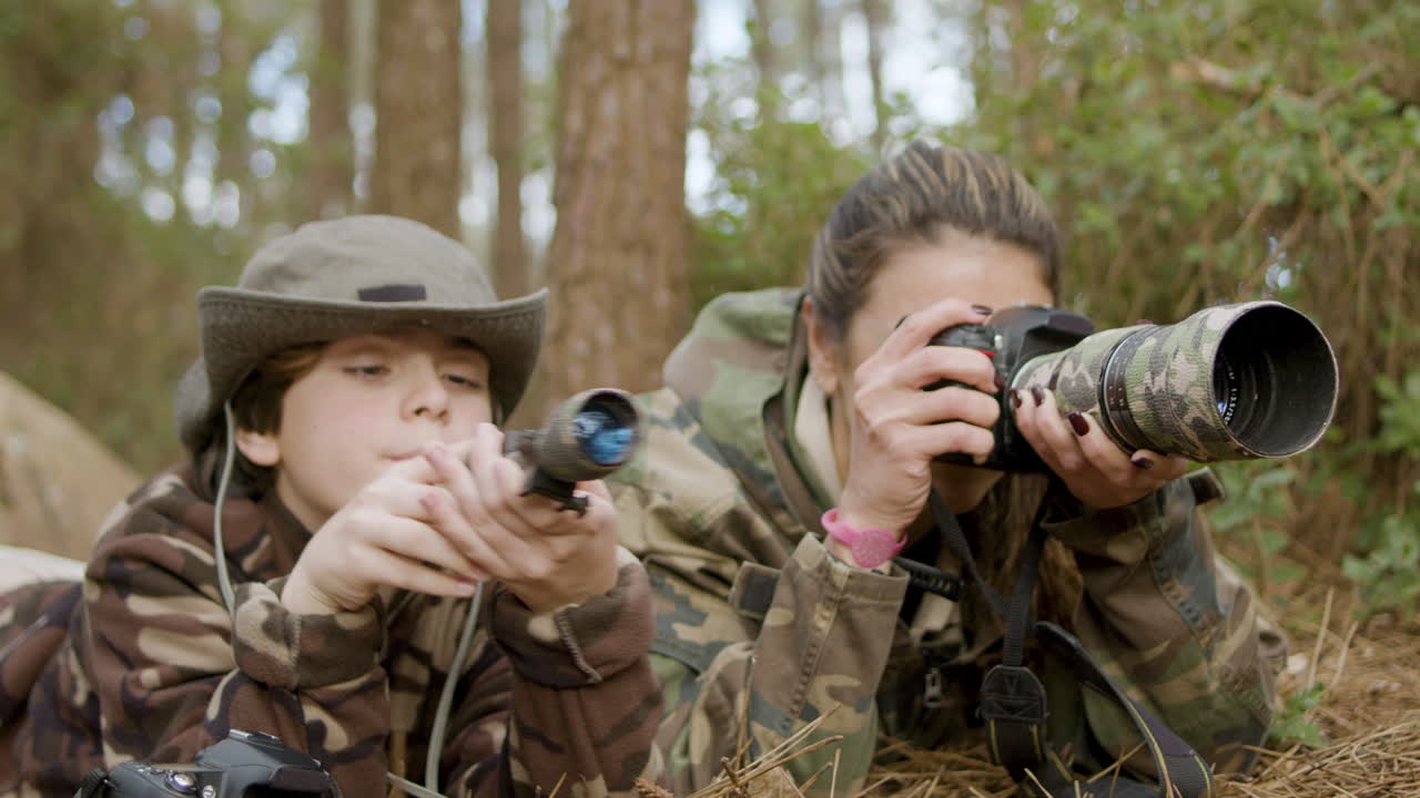 кавказская женщина и ее сын наблюдают за птицами, лежа на земле в лесу