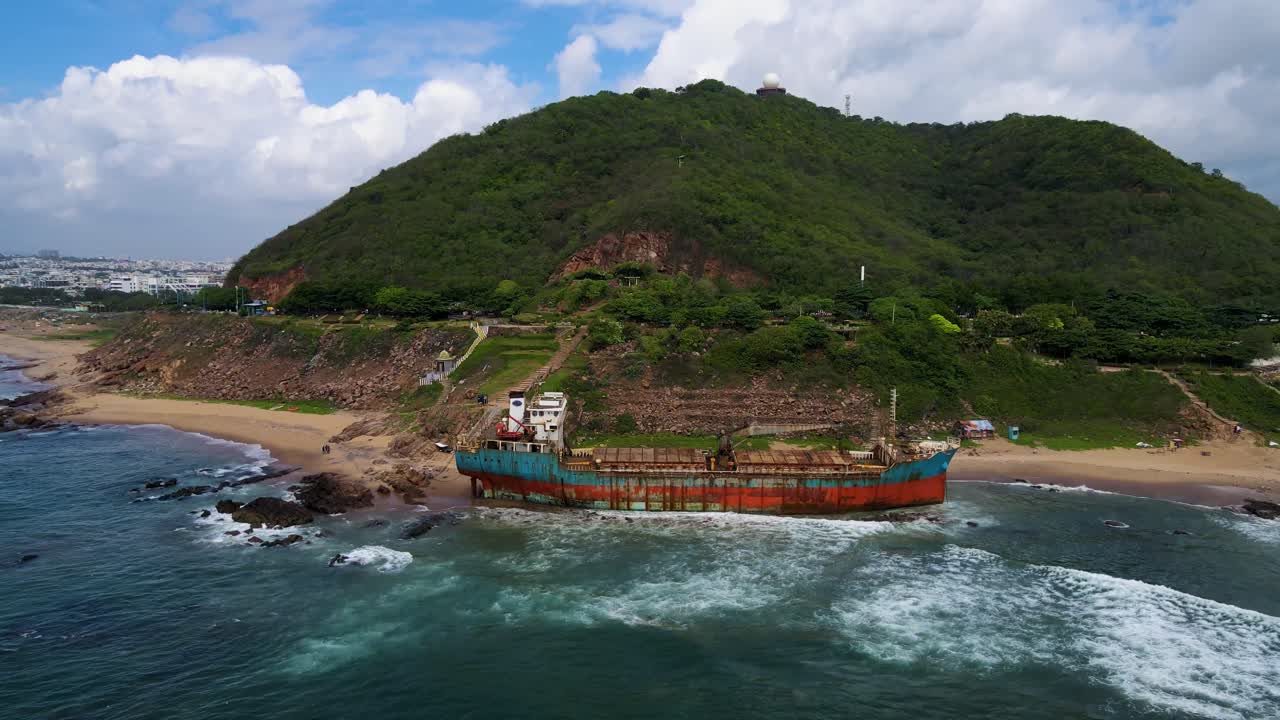 Breathtaking aerial drone shot of a shipwreck off Vizag's coastline, with waves crashing around the wreckage.