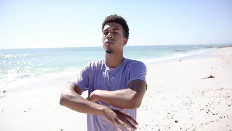 Un-Joven-Birracial-Se-Encuentra-Con-Los-Brazos-Cruzados-En-Una-Playa-Soleada.