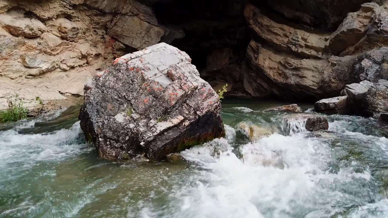 A drone shot backing up from a cavern with rushing water flowing. (slow motion)