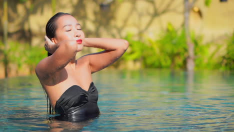 Sexy-young-woman-strokes-her-wet-hair-in-pool-while-looking-at-camera