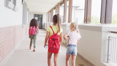 video de vista trasera de niñas diversas caminando en el pasillo de la escuela y hablando