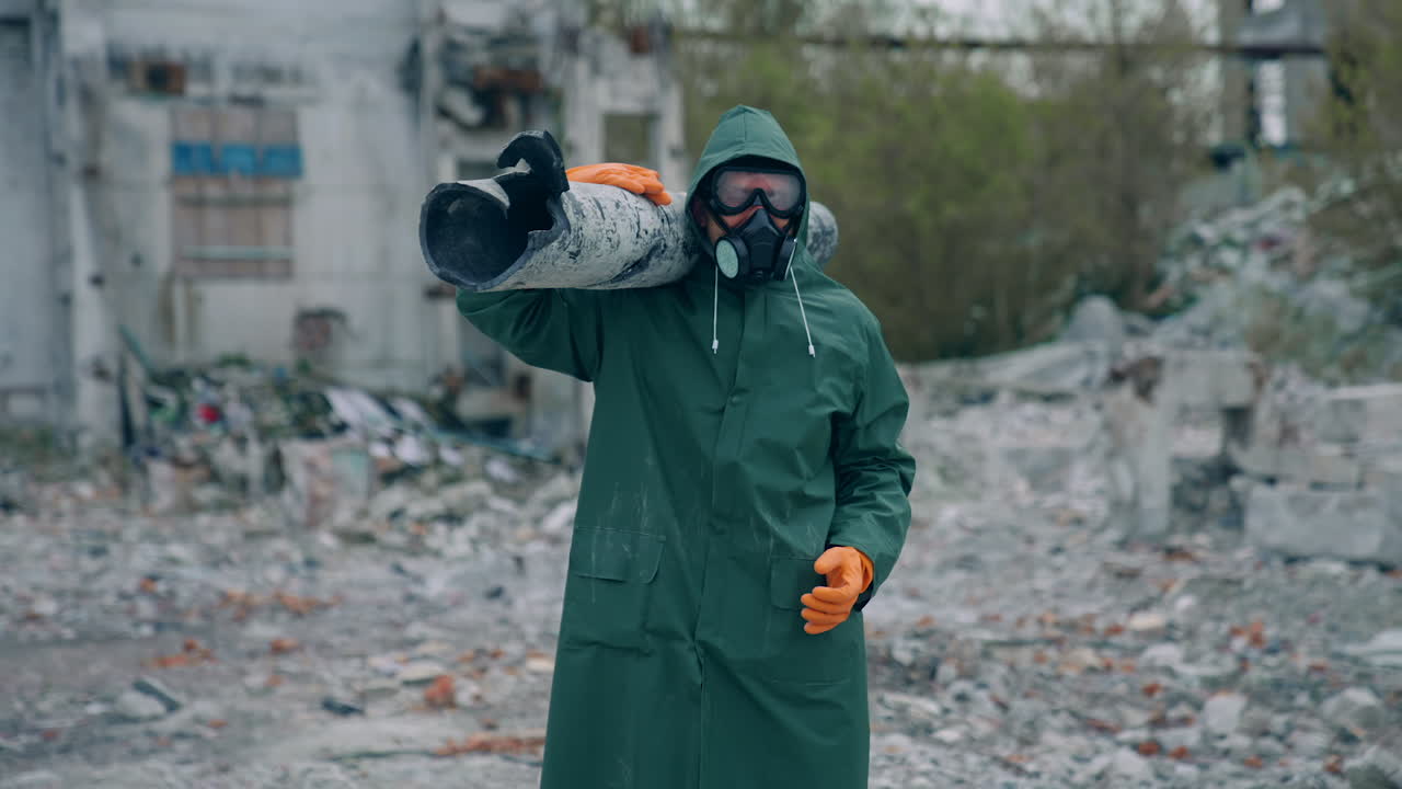 Worker in protective suit in radiation zone. Builder in safety uniform and gas mask is carrying pipe in destroyed place. Chemical attack.