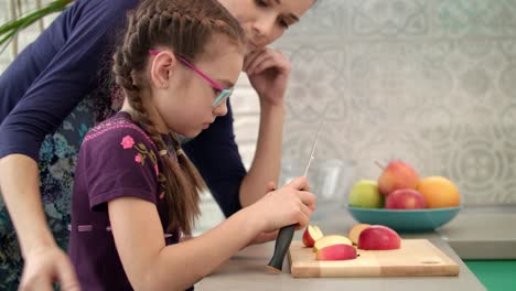 madre aprendiendo a su hija usando un cuchillo. niña cortando una rebanada de manzana