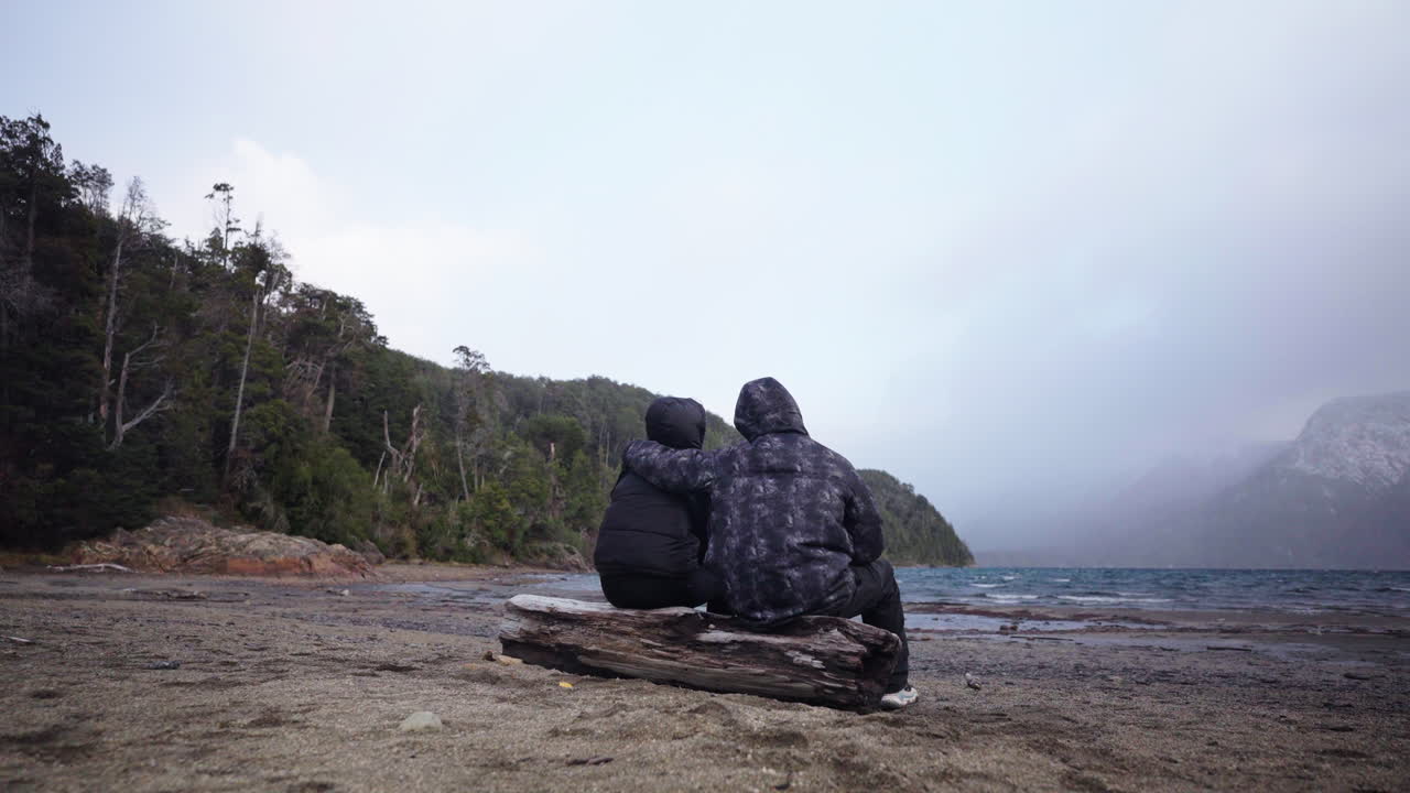 Father hugs his son in gesture of support while sitting on log on empty exotic beach